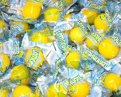several yellow individually wrapped lemonheads flavored hard candies, each covered in clear plastic packaging with blue and green text.
