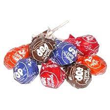A pile of assorted Tootsie Roll Pops bulk in different flavors, including chocolate, orange, and raspberry, with colorful wrappers