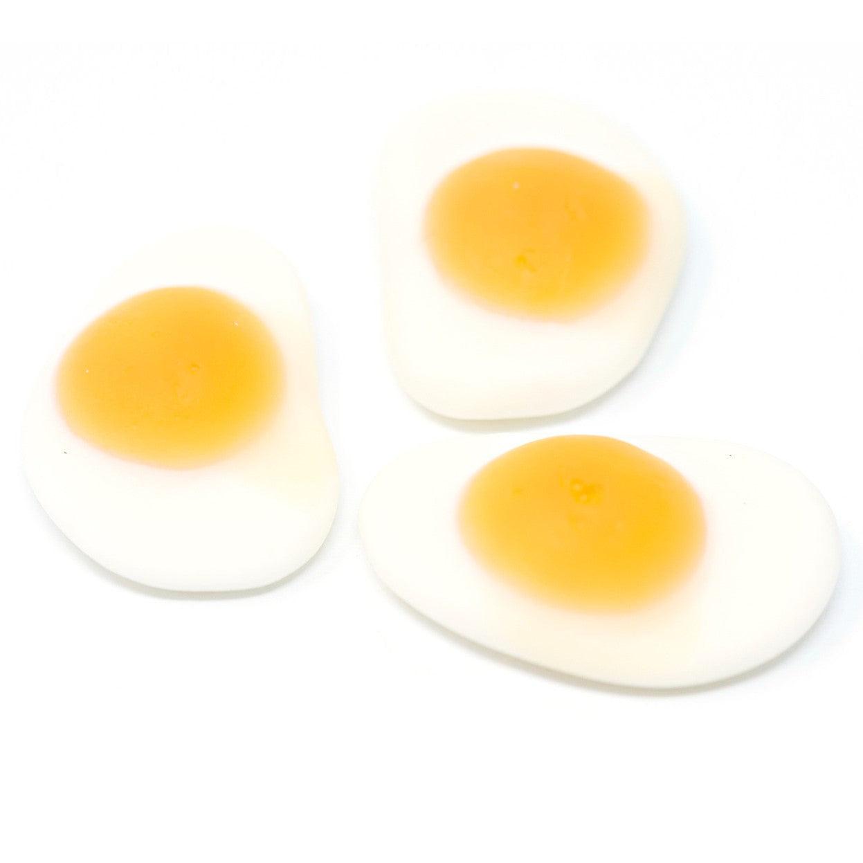 Three vidal gummy fried eggs, with white "egg whites" and yellow "yolks" on a white background.